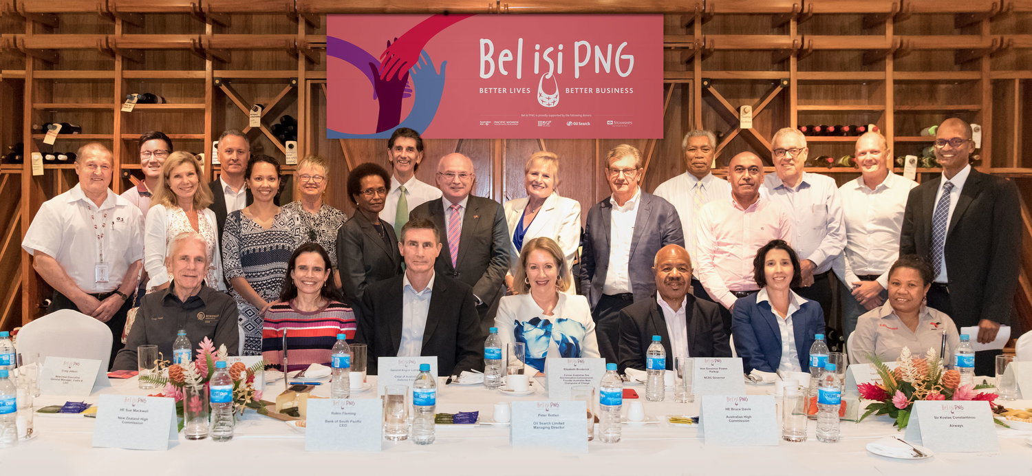 Group of people pictured seated and standing in front of the Bel isi PNG banner.