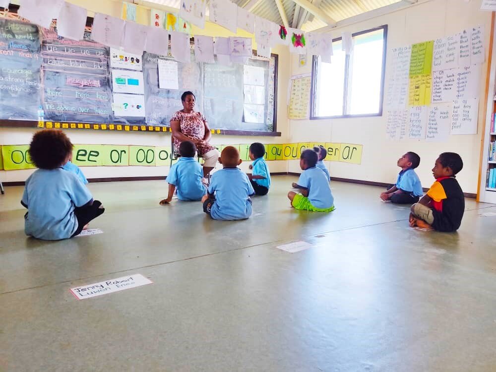 young children sitting on the floor in front of a teacher in a library classroom