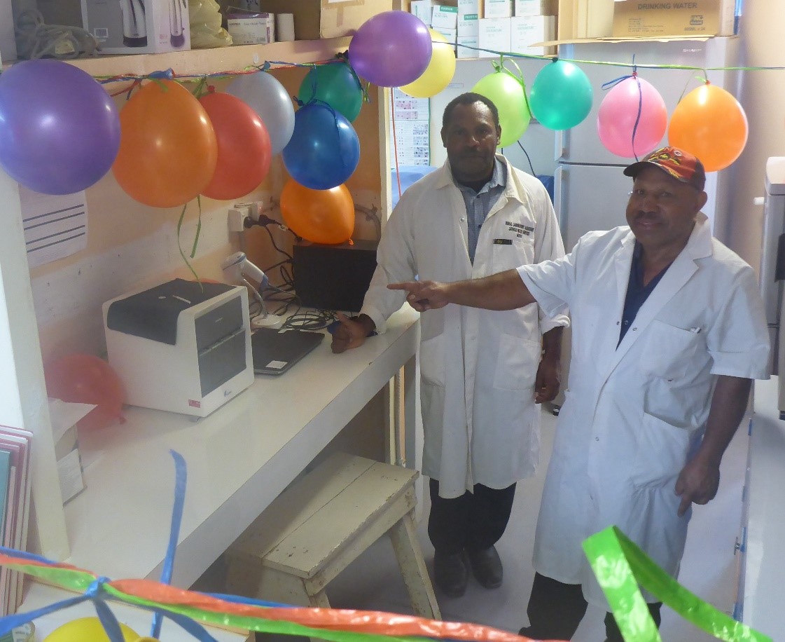 Two doctors standing next to GeneXpert Machine with balloons celebrating the installation.