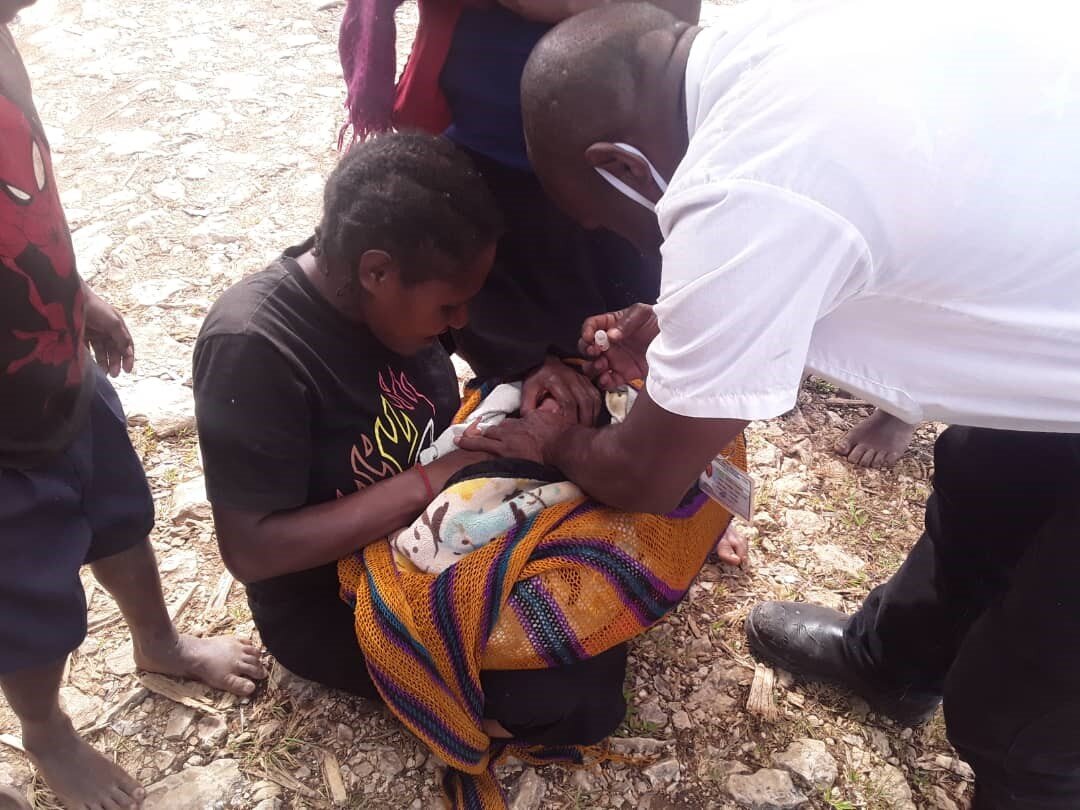 Health care worker in white shirt administering immunisation to newborn baby wrapped in orange blanket